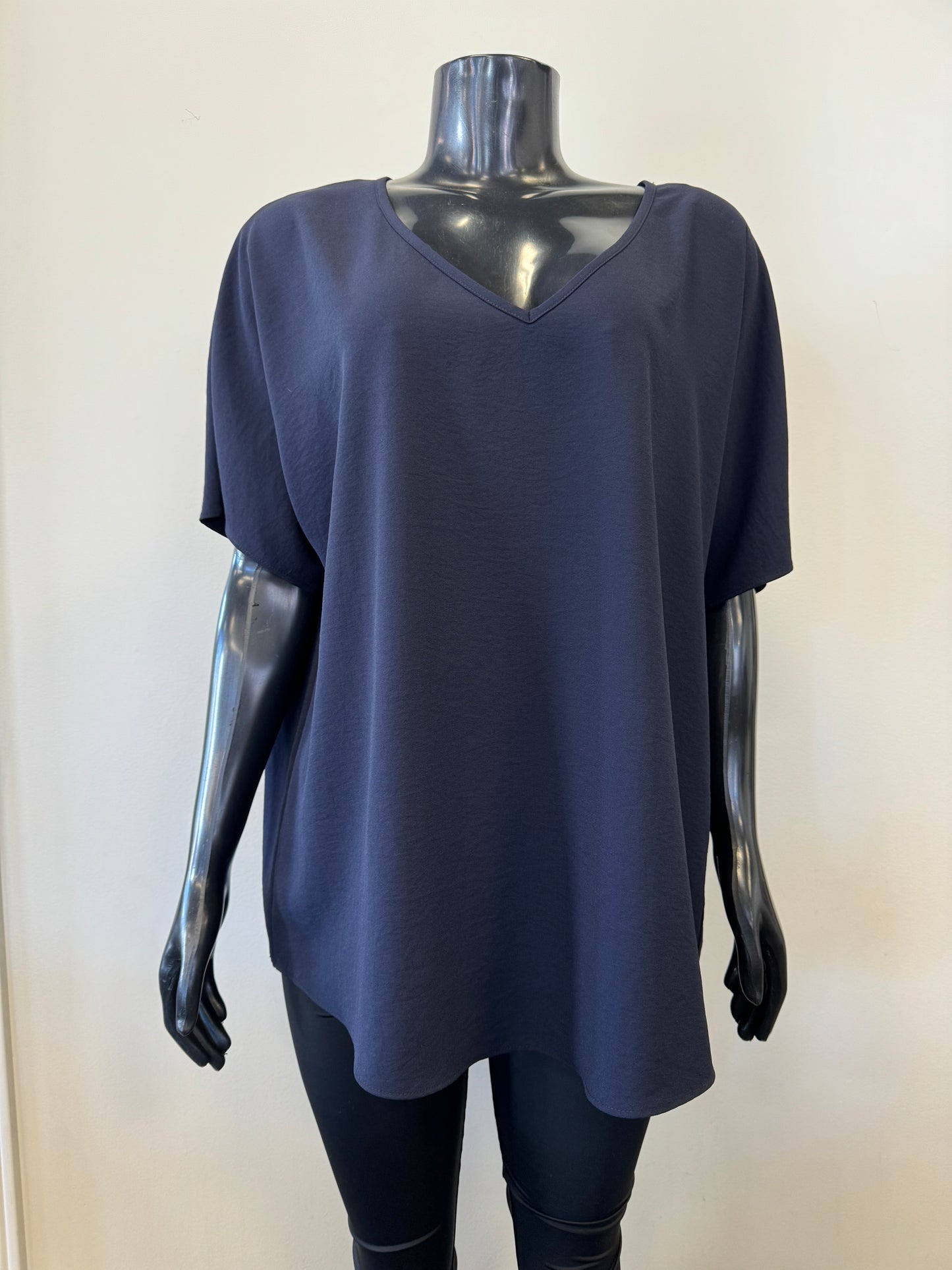 A black mannequin showcases a simple, loose-fitting white V-neck T-shirt with short sleeves and a relaxed fit, known as the Loose V-neck Top Style 231002 by Joseph Ribkoff. The slouchy top is set against a plain, light-colored background.