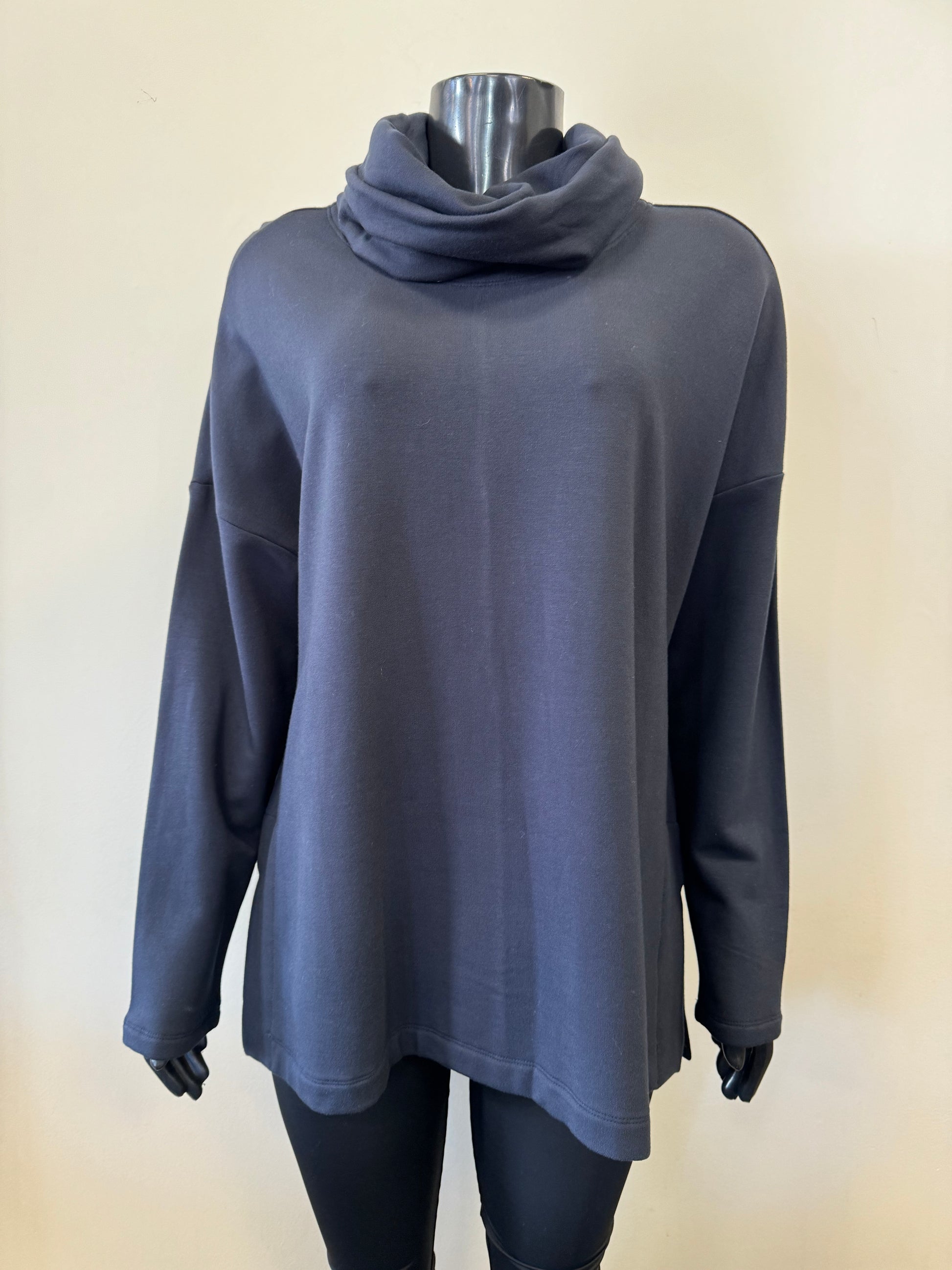 A mannequin dressed in a dark gray FOIL Cosy Up Cowl Sweat FO6684 and black fitted pants. The sweatshirt, from FOIL, features a relaxed fit with dropped shoulders. The background is a plain light-colored wall.