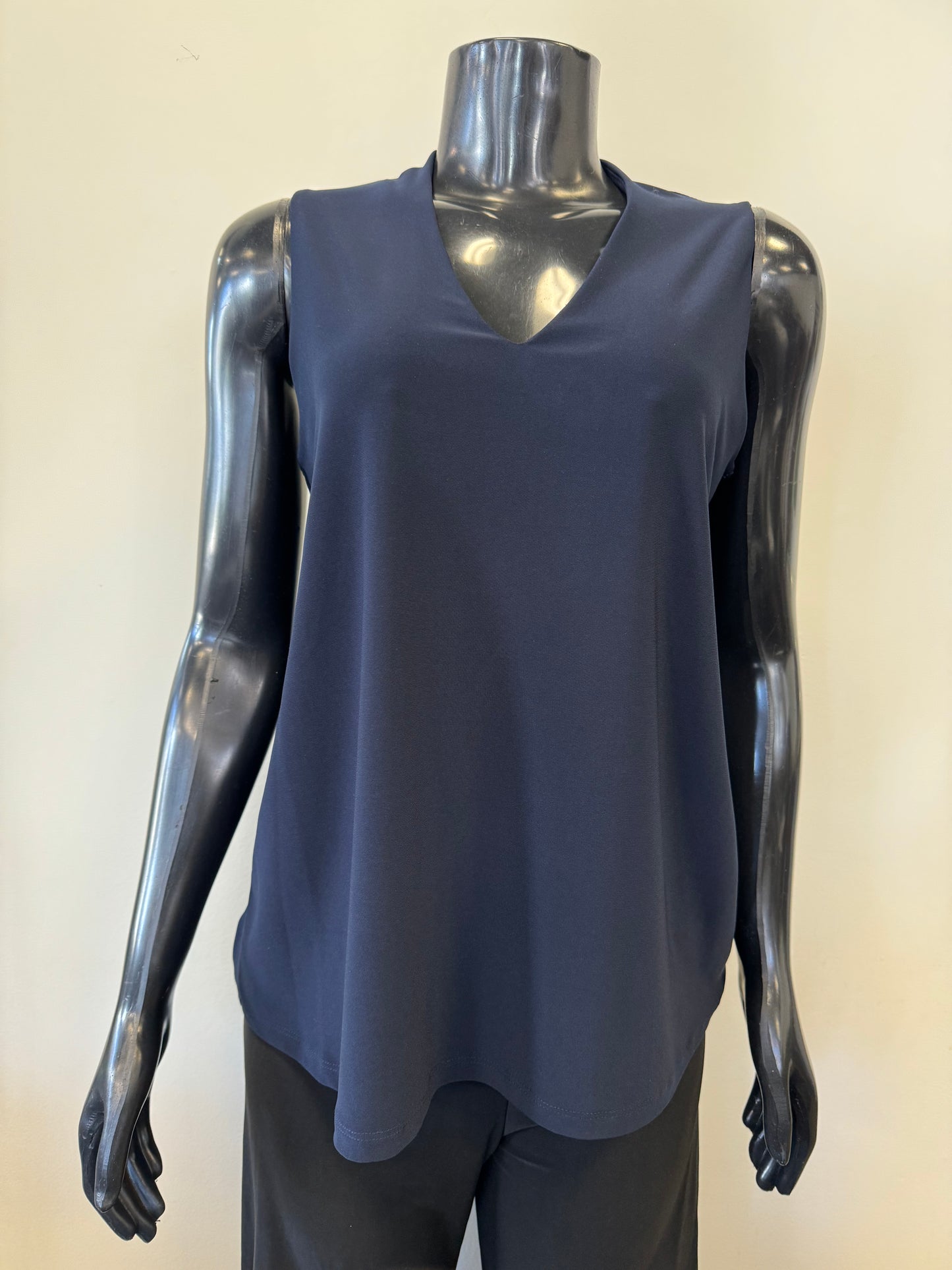 A black mannequin displays a sleeveless, deep V-neck, navy blue Bali Corp Bali Top Sleeveless 8326 paired with black trousers. The versatile top is made in Canada and stands out against the plain, white background.