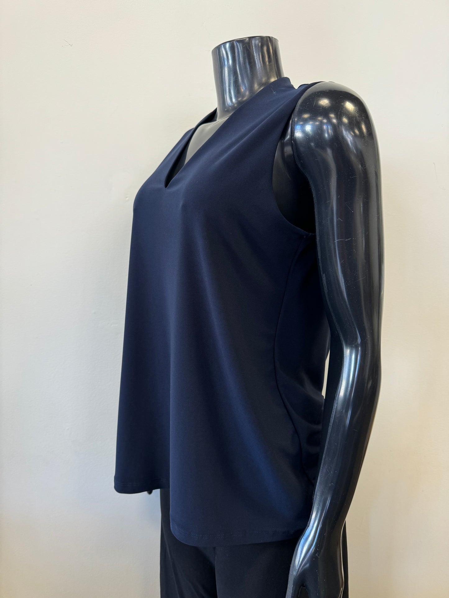 A black mannequin displays a sleeveless, deep V-neck, navy blue Bali Corp Bali Top Sleeveless 8326 paired with black trousers. The versatile top is made in Canada and stands out against the plain, white background.