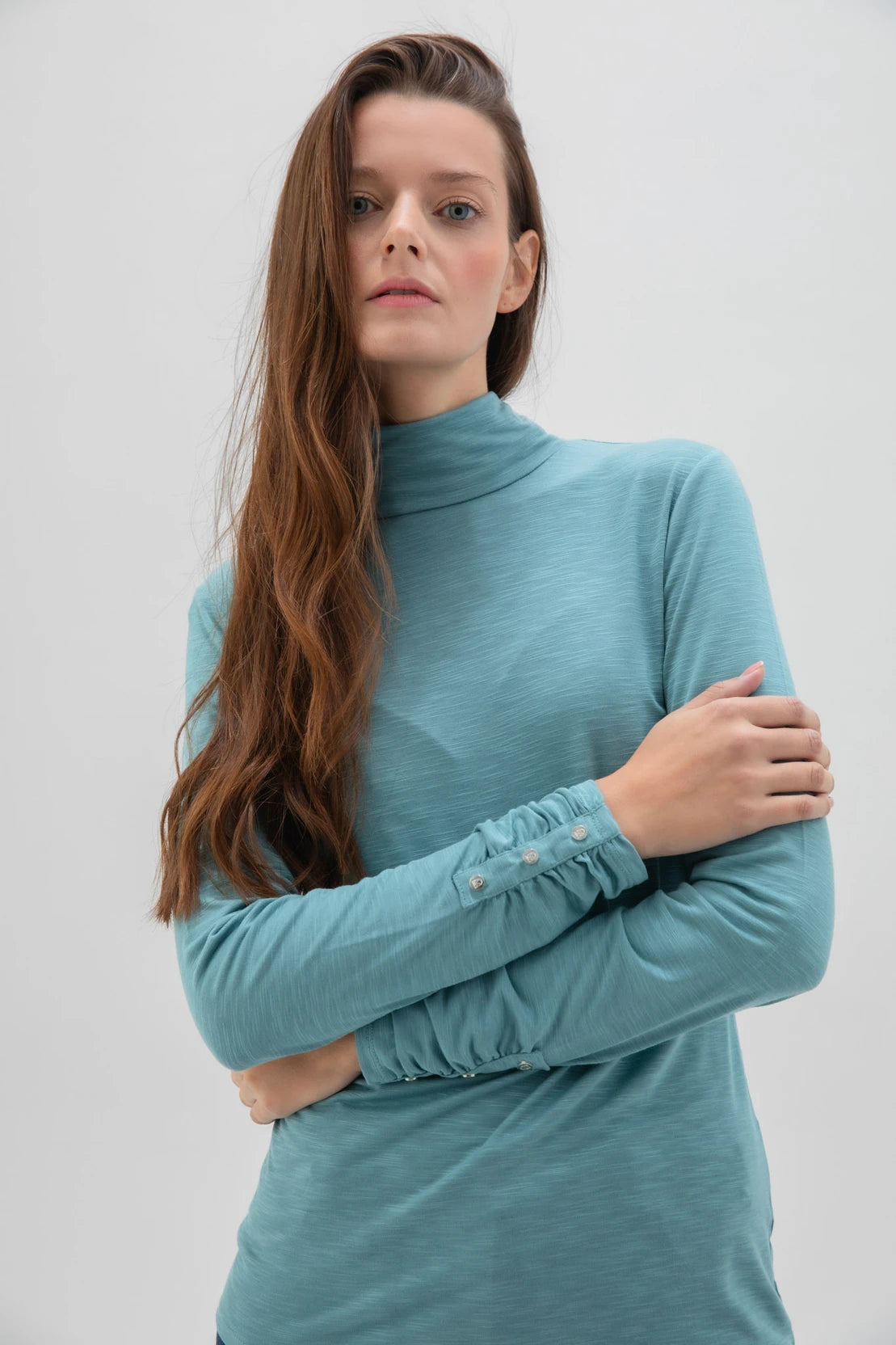 The Marble L/S Turtleneck Top w/Ruche Cuff & Button Detail by MARBLE is showcased against a white background. This plain, white long sleeve turtleneck features a fitted design and is crafted from a viscose blend. The top is distinguished by ruched cuffs adorned with button details near the wrists.