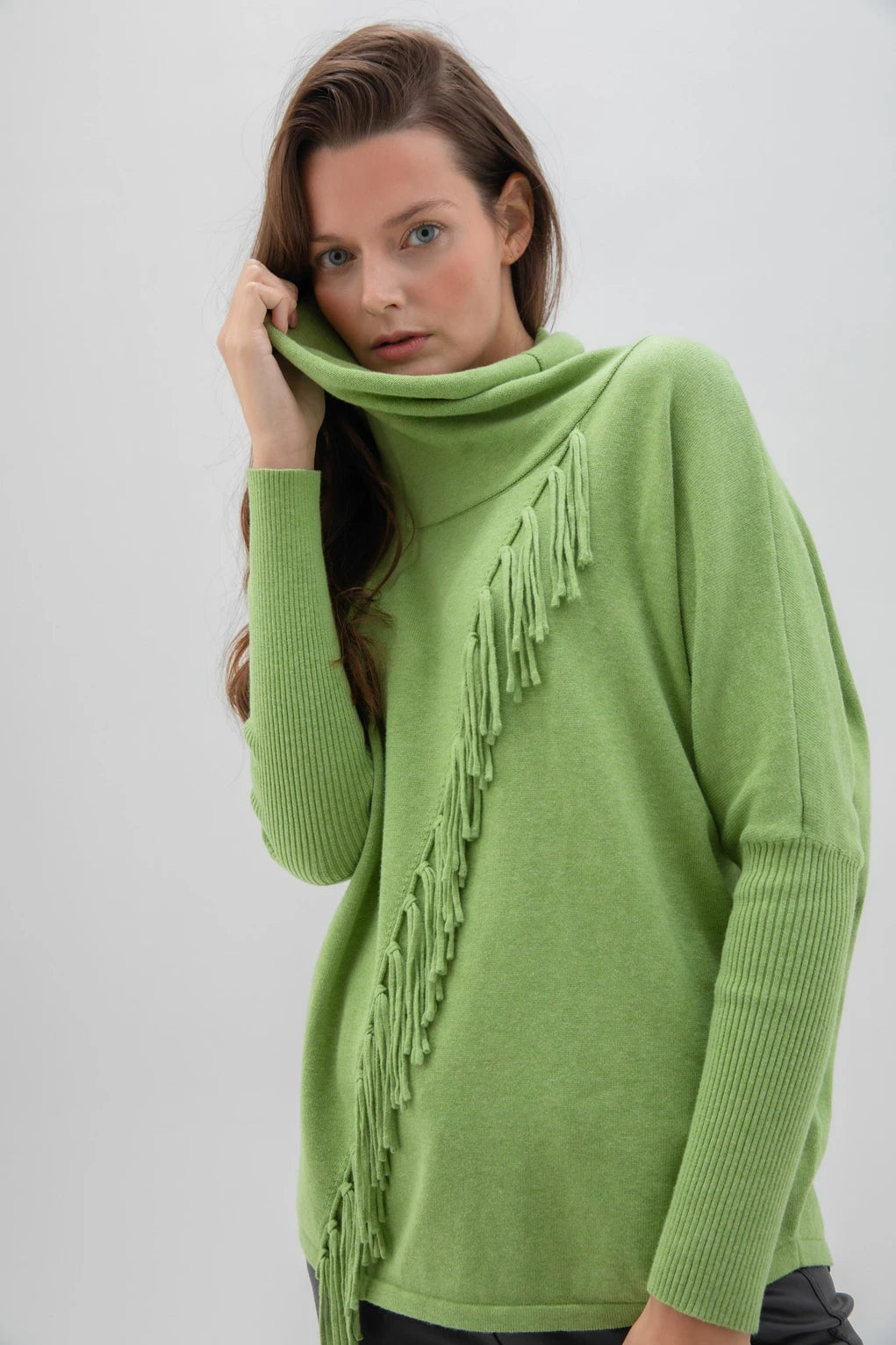 The Marble brand product, Sweater 6373-104 MARBLE, is a white, long-sleeved cotton sweater featuring a cowl neck and decorative fringe detailing that starts from the neckline and runs diagonally across the front. This high-quality sweater has a relaxed fit and ribbed cuffs on the sleeves.