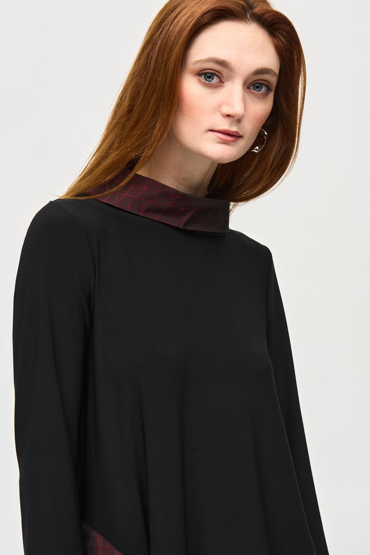 A woman with long red hair stands against a plain background, wearing the Silky Knit And Memory Cocoon Dress 243080 by Joseph Ribkoff. The dress features dark red accents on the pockets and hem, which she pairs with black knee-high boots. She has a confident expression and her hands in her dress pockets.