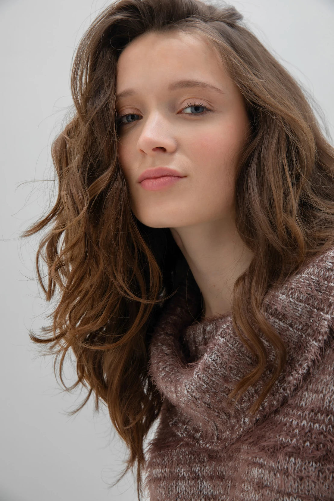 A woman with long, wavy brown hair is wearing a fashionable and cozy Sweater 7544 MARBLE by MARBLE. The fuzzy brown sweater features a stylish cowl neck. She is standing against a plain white background and looking forward with a neutral expression.