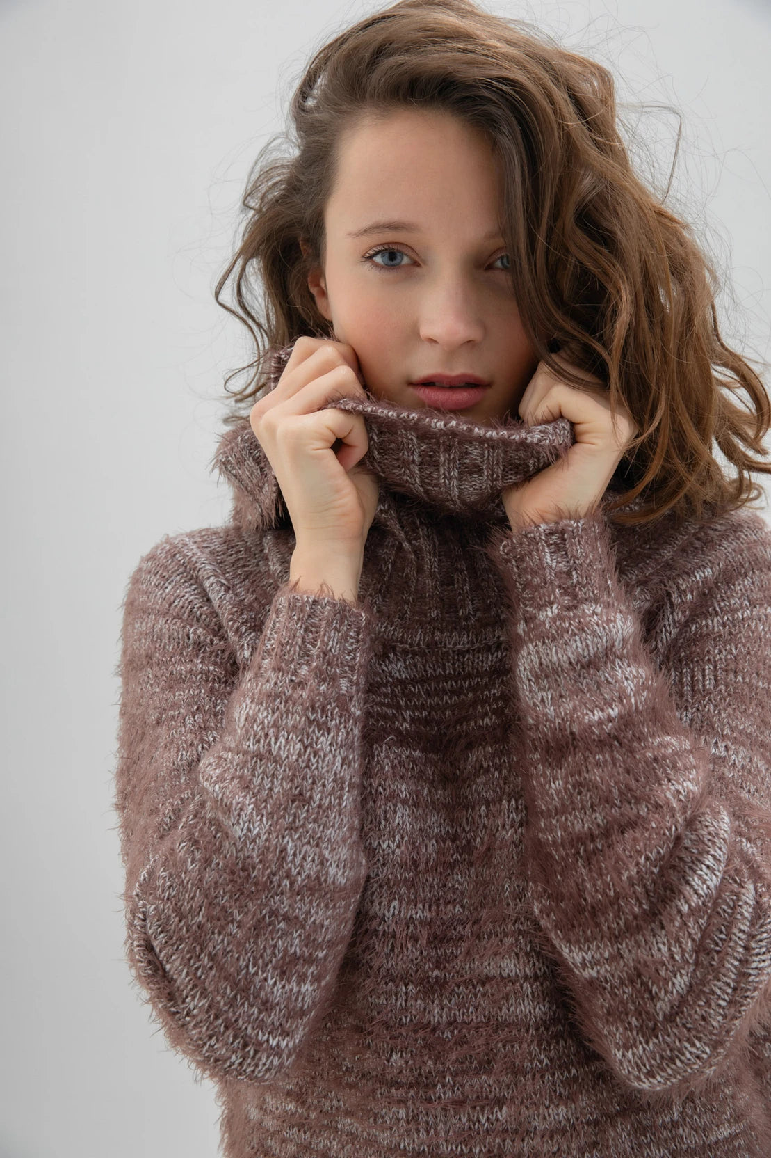 A woman with long, wavy brown hair is wearing a fashionable and cozy Sweater 7544 MARBLE by MARBLE. The fuzzy brown sweater features a stylish cowl neck. She is standing against a plain white background and looking forward with a neutral expression.