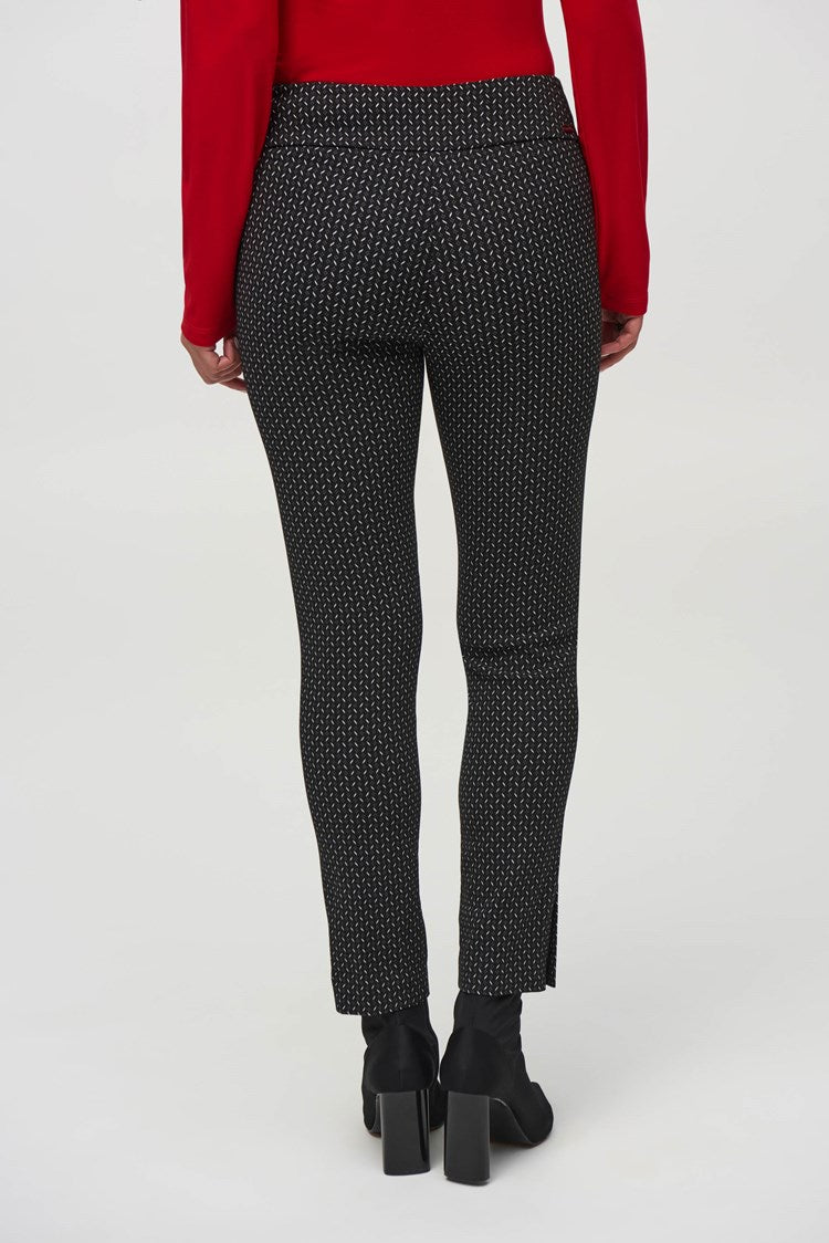 A woman wearing a fitted red long-sleeve top, paired with Joseph Ribkoff's Jacquard Abstract Print Pull-On Pants (style 244140), and ankle-length black boots stands against a plain white background. She has shoulder-length dark hair and is looking directly at the camera with a neutral expression.