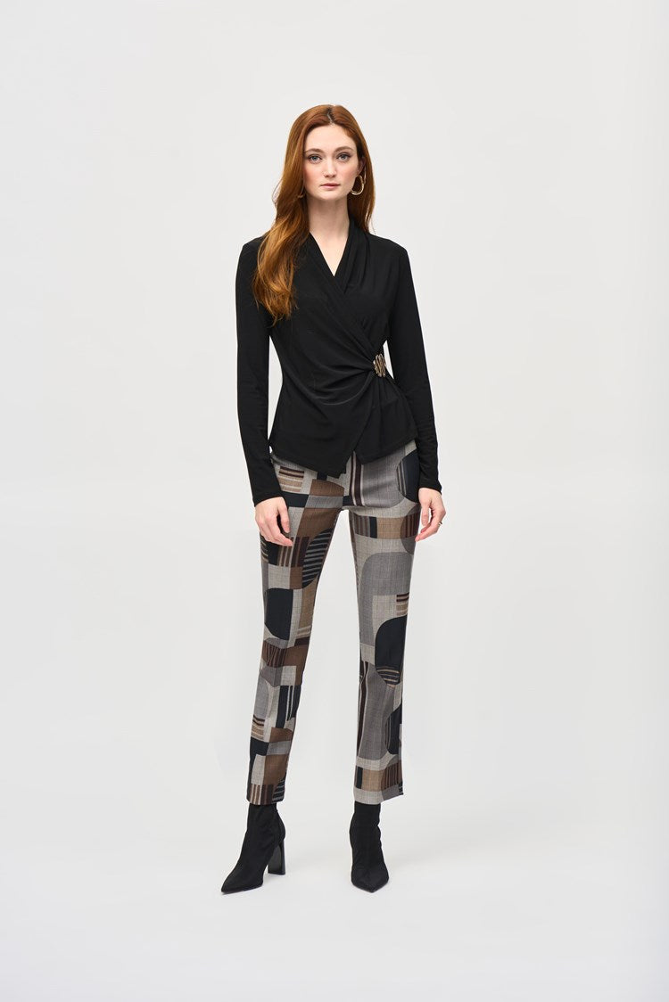 A woman stands against a plain white background, wearing a black wrap-style top with long sleeves and Jacquard Abstract Print Straight Pull-On Pants 243299 by Joseph Ribkoff, featuring abstract patterns in shades of brown, gray, and black. She completes the outfit with black ankle boots. She has long, reddish-brown hair and a neutral expression.