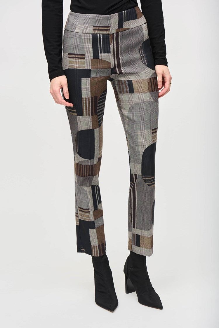 A woman stands against a plain white background, wearing a black wrap-style top with long sleeves and Jacquard Abstract Print Straight Pull-On Pants 243299 by Joseph Ribkoff, featuring abstract patterns in shades of brown, gray, and black. She completes the outfit with black ankle boots. She has long, reddish-brown hair and a neutral expression.