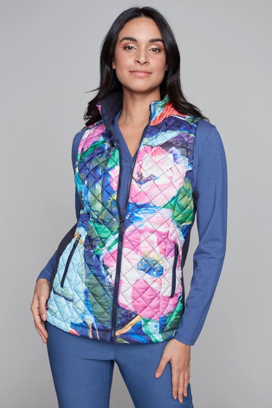 A woman with long dark hair stands against a gray background, donning the vibrant and stylish Woven Vest 91715 Clare Desjardins by Claire Desjardins over a blue long-sleeve top. One hand is in her pocket, and she looks confidently at the camera.