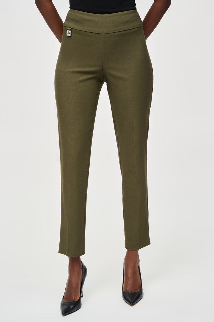 A woman stands confidently, wearing a black three-quarter sleeve blouse with patterned details at the hem and Classic Slim Pant - Seasonal Colors 201483F24 Joseph Ribkoff in olive green. She pairs the outfit with black high-heels and hoop earrings. The background is plain white.