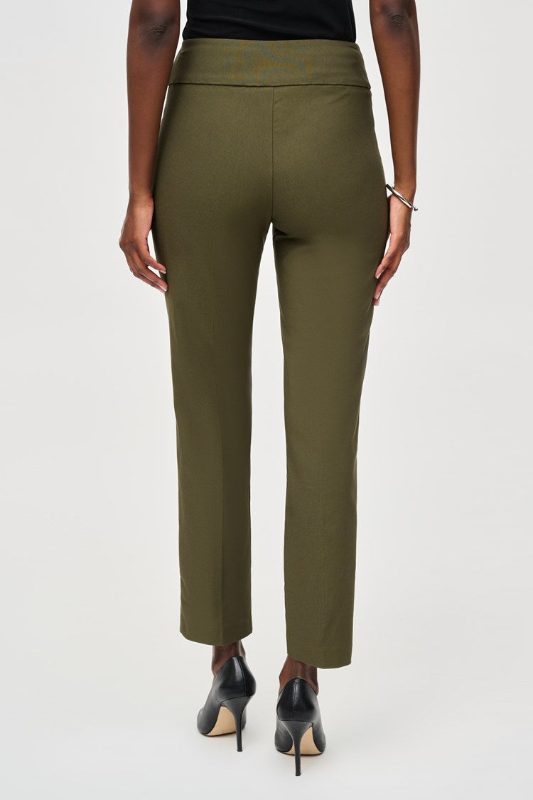 A woman stands confidently, wearing a black three-quarter sleeve blouse with patterned details at the hem and Classic Slim Pant - Seasonal Colors 201483F24 Joseph Ribkoff in olive green. She pairs the outfit with black high-heels and hoop earrings. The background is plain white.