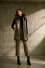 A person with long dark hair stands against a concrete wall, wearing the Joseph Ribkoff Quilted Hooded Puffer Vest over a black top and taupe pants, paired with black ankle boots. With their hands in the vest pockets and looking directly at the camera, this outfit is perfect for the cooler seasons.