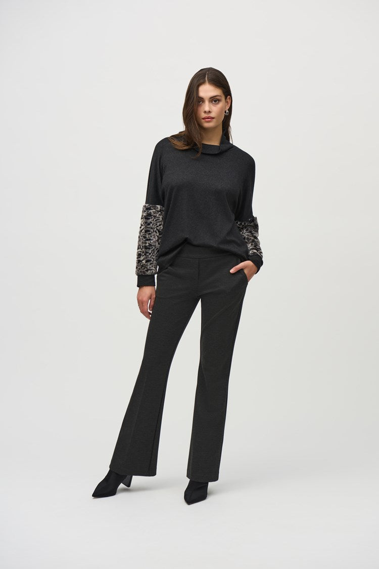 A woman with long hair stands against a plain white background. She is wearing a black long-sleeve top with leopard print accents on the sleeves and Joseph Ribkoff's dark gray Denim Straight Pants With Frayed Hem cropped to the ankle. She pairs the outfit with black pointed-toe shoes.