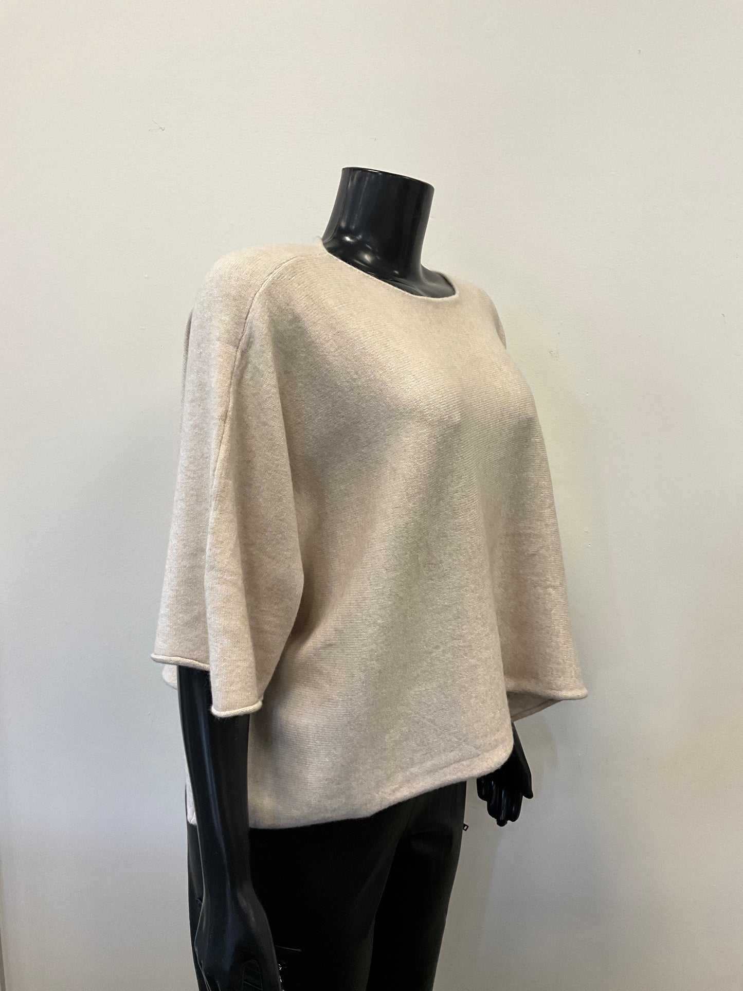 A mannequin dressed in a loose-fitting, light beige Sweater Round Neck - Eternelle made from premium fabrics with three-quarter-length sleeves. The ETERNELLE brand top is paired with black pants. The mannequin stands against a plain, light-colored background.