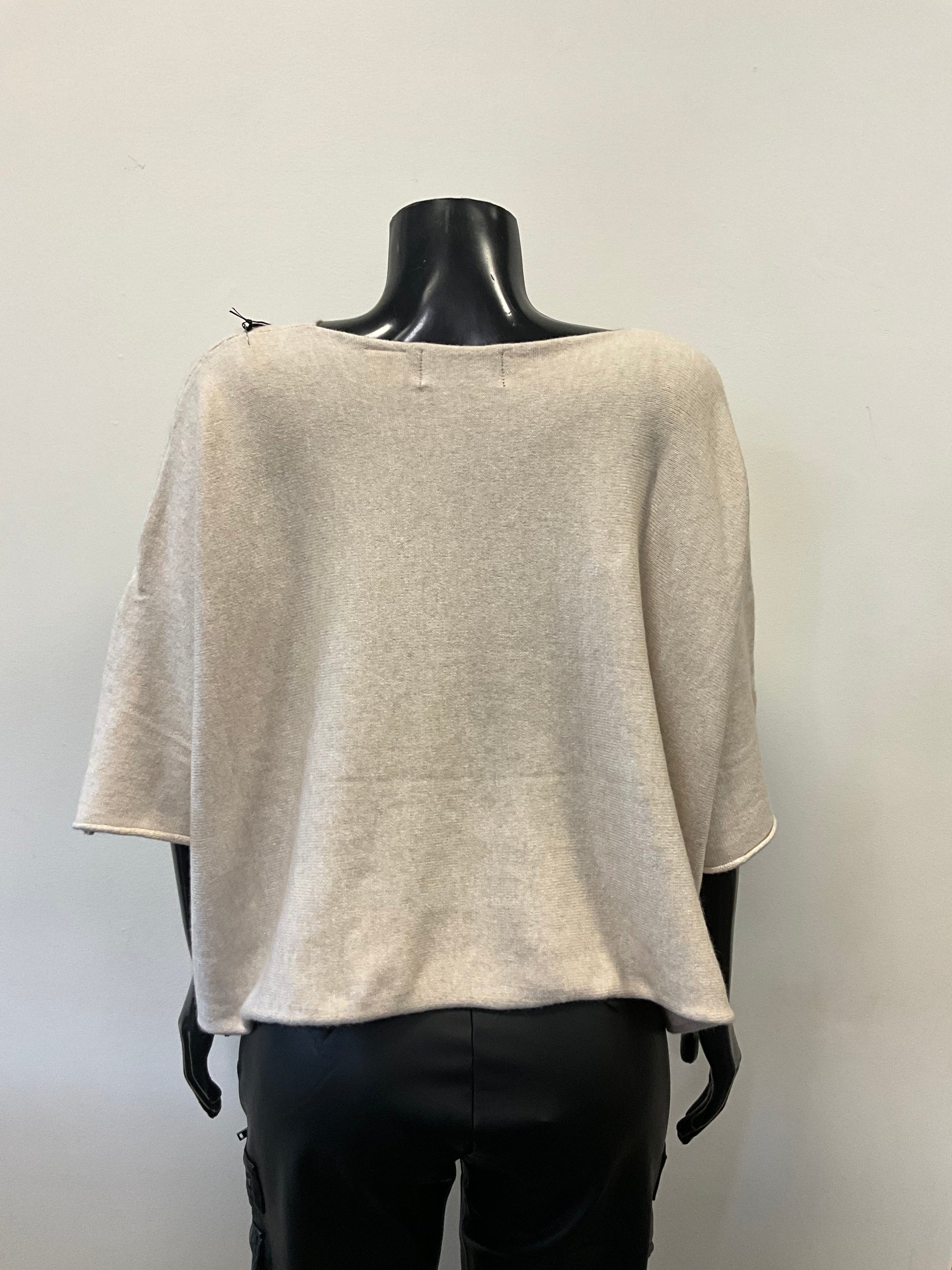 A mannequin dressed in a loose-fitting, light beige Sweater Round Neck - Eternelle made from premium fabrics with three-quarter-length sleeves. The ETERNELLE brand top is paired with black pants. The mannequin stands against a plain, light-colored background.