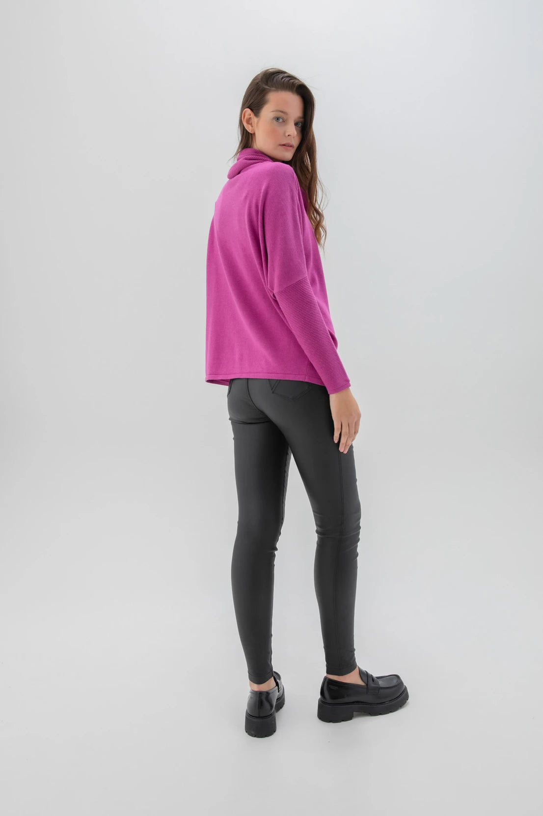 A woman stands against a plain background wearing the MARBLE Marble Sweater-6727, which features large buttons along the side, paired with black leggings and black shoes. Her long hair is styled to one side, and she faces the camera with a neutral expression.