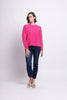 A person with short hair is standing against a plain background, wearing a bright pink, fuzzy "Fluff Love Sweater - FOIL" by FOIL, dark blue jeans, and beige slip-on shoes. The person has one arm relaxed at their side and the other slightly bent with their hand near their hip.