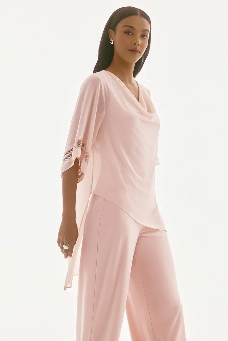 A woman wearing the Signature Chiffon Asymmetrical Layered Top 251740 by Joseph Ribkoff, featuring a light pink draped design with lace accents on the sleeves and a chiffon overlay, paired with matching wide-leg pants. She has long, straight hair and stands against a plain white background.