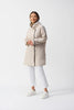 Wearing the Memory Hooded Trapeze Coat 251184 by Joseph Ribkoff, a person stands against a white background with relaxed arms. The light beige coat features contrast binding and a high collar, paired with white pants and sneakers for an effortlessly chic, vintage-inspired look.