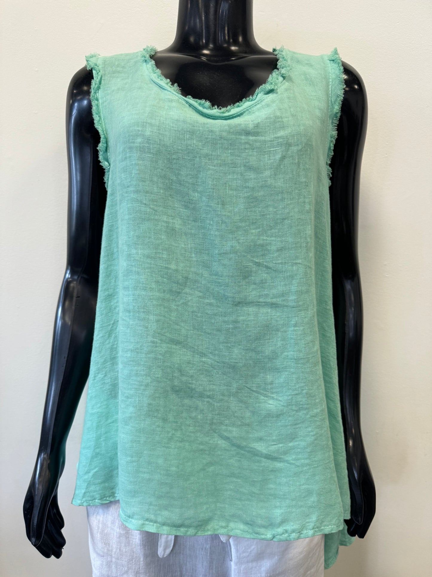 A black mannequin is wearing a Tea Green sleeveless linen top with a frayed neckline and armholes from the Catherine Lillywhite collection. The high-quality Sleeveless Linen Top - TEA Catherine Lillywhite features a loose fit that is perfect for warm weather, paired with white bottoms. The background is plain white.