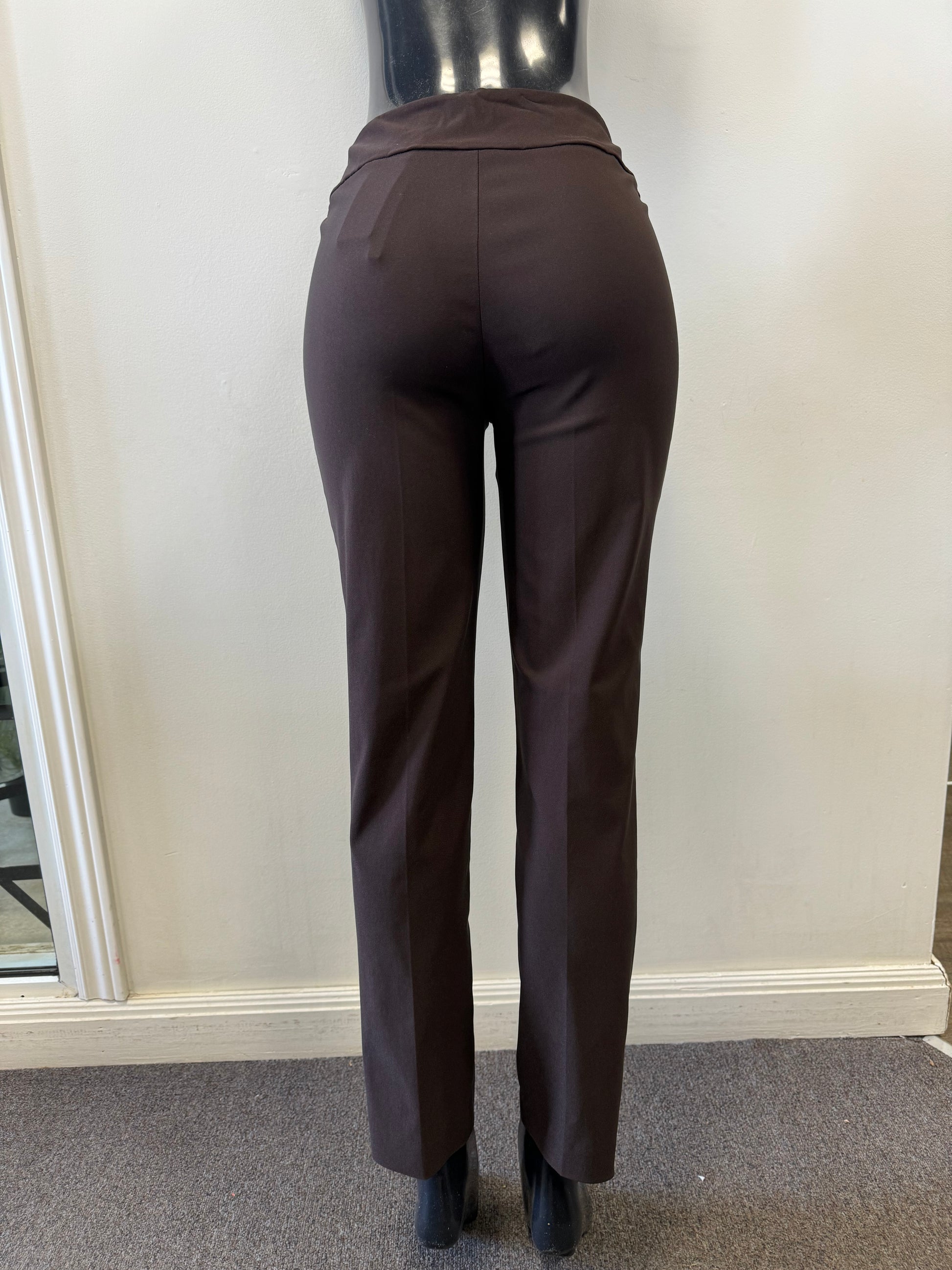 A pair of Joseph Ribkoff Pants Style 201483TT MOCHA in dark brown is displayed on a black mannequin against a plain white wall. These dressy yet comfortable trousers feature a high waist and front seam detailing, with a small pocket visible on the right side. The mannequin stands on a grey carpeted floor.