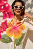 Someone in white sunglasses adjusts their collar, wearing a Joseph Ribkoff embroidered flower cotton shirt. Bright pink flowers blur in the foreground, adding vibrant touches to the sunny scene.