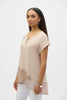 A woman poses against a white background in a Joseph Ribkoff silky knit asymmetrical top with a keyhole neckline and foiled mesh hem (Product 252172), paired with white pants, large hoop earrings, and a bracelet.