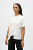 A woman effortlessly embodies casual chic, wearing Joseph Ribkoff's Jersey And Seersucker Asymmetrical Top 252117 against a plain white background, paired with black pants. Her long, dark hair complements hoop earrings and a bracelet, with her expression remaining neutral.