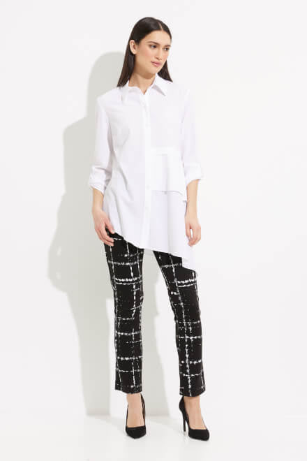 A person with long dark hair is wearing a white Joseph Ribkoff Tiered Asymmetric Hem Blouse Style 233099, which features asymmetric layers on the front and 3/4 sleeves. Paired with black pants adorned with a white grid pattern, this stylish ensemble by Joseph Ribkoff is perfect for an office wardrobe. The background is plain white.