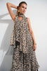 A woman stands against a white backdrop wearing the Joseph Ribkoff Chiffon Animal Print Reversible A-Line Tunic 252155, featuring fringed edges. She complements the look with a matching scarf, large hoop earrings, and gold bangles, striking an elegant pose with her raised right arm.