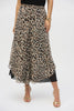 A person stands confidently in Joseph Ribkoff's Chiffon Animal Print Reversible Culotte Pants, paired with a black top, gold bracelets, and chic gold high-heeled sandals. Their hand rests stylishly on their waist against a plain white background.