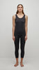 A person with long brown hair stands facing forward against a plain white background. They are wearing a black sleeveless top and the UCHUU BASIC LEGGINGS - CS24-104 by UCHUU, made of nylon, and they are barefoot. The image suggests a minimalist, neutral style.