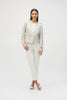 A model poses against a plain white background, wearing the Joseph Ribkoff Foiled Faux Suede Boxy Jacket in light gray with large metal snap buttons. The ensemble is completed with matching faux suede pants and open-toed shoes, standing with one leg slightly forward and hands at their sides.