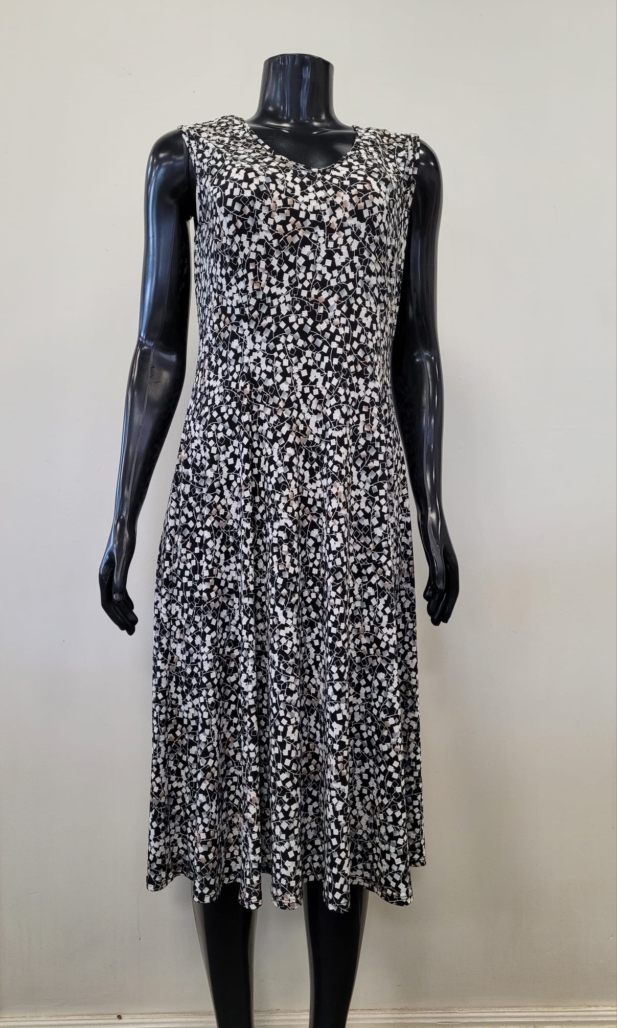 The Breezy Dress 8580-Bali Corp by Bali Corp is a sleeveless, knee-length black summer dress with a white and beige floral pattern, shown on a black mannequin against a light background. Ideal for cute summer outfits.