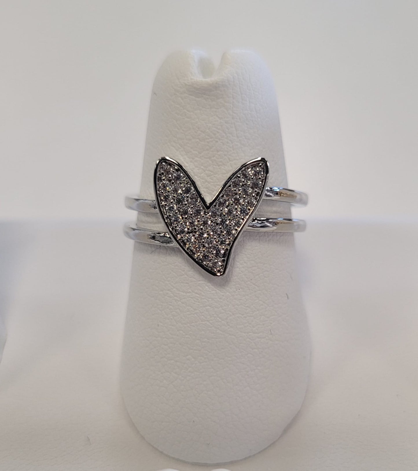 The Kristin 27 Ring by Elise Accessories features a heart-shaped design with small clear stones, displayed elegantly on a white ring stand against a plain background.