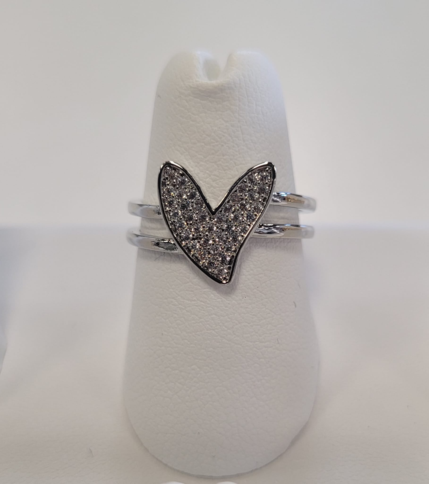 The Kristin 27 Ring by Elise Accessories features a heart-shaped design with small clear stones, displayed elegantly on a white ring stand against a plain background.