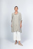 Against a plain backdrop, a person dons a loose gray polka dot tunic with white pants and casual taupe slip-ons by Paolo Tricot, exuding effortless Italian style.