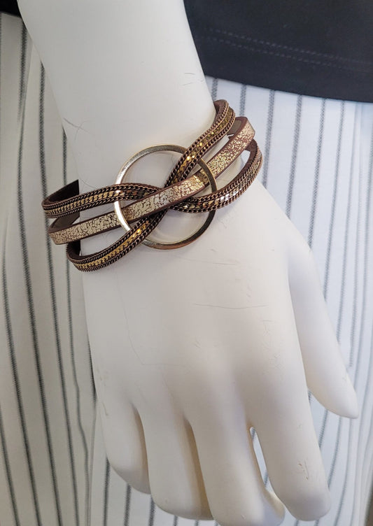 A mannequin hand displays the Clara 15 Bracelet by Elise accessories, with multiple strands looping through a central gold ring, set against black and white vertical stripes—a magnetic piece that adds modern flair to any outfit.