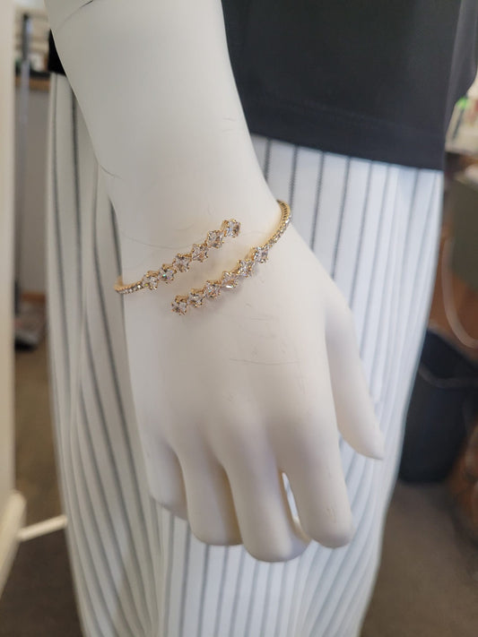 A mannequin hand wears two elegant gold bracelets, including the Elise accessories Mimosa 11 Bracelet with sparkling crystals, styled against a black top and a white skirt with vertical black stripes.