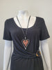 A mannequin in a black short-sleeve top with a side buckle wears the Elise accessories Sofia 13 Necklace, featuring a large pink enamel heart pendant outlined in silver.