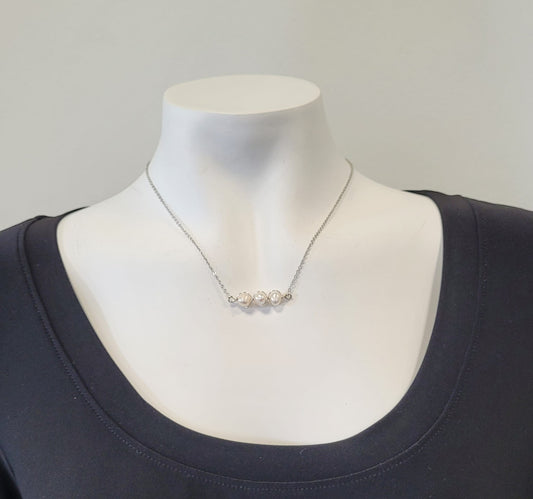The Trina Necklace by Elise Accessories, featuring three white freshwater pearls and silver tones, is showcased on a white mannequin in a black scoop-neck top against a plain light background.