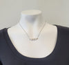The Trina Necklace by Elise Accessories, featuring three white freshwater pearls and silver tones, is showcased on a white mannequin in a black scoop-neck top against a plain light background.