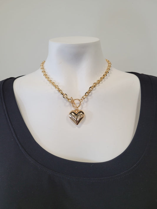 The Fiona 24 Necklace by Elise accessories features a shiny gold heart pendant on a gold chain, elegantly displayed on a white mannequin dressed in a plain black top.