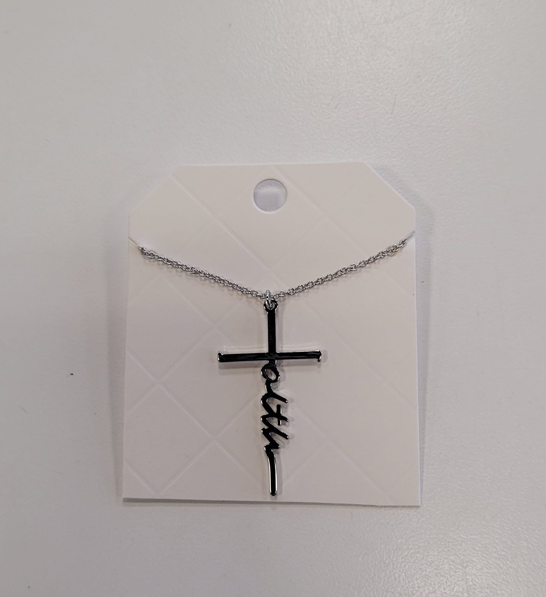 The Trina 13 Necklace by Elise accessories features "faith" woven into a silver cross, displayed on a diamond-patterned white card—a stylish addition to any collection.