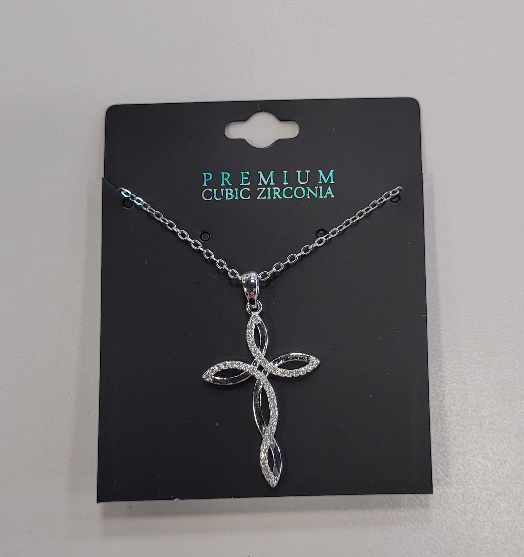 The Trina 12 Necklace by Elise Accessories features a silver figure 8 cross with sparkling cubic zirconia on black "Premium Cubic Zirconia" packaging. Its elegant, intertwined design is perfect for layering with your favorite necklaces.