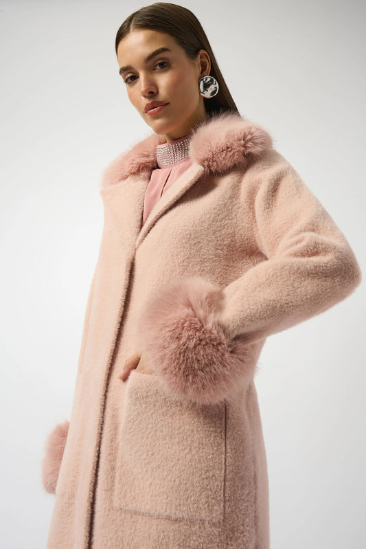 A woman models the Joseph Ribkoff Feather Yarn and Faux Fur Sweater Coat 243923F25 in light pink, featuring cozy faux fur trim on the cuffs and collar, posing confidently with one hand in her pocket against a white background.