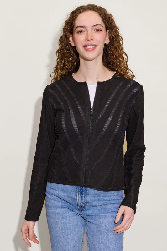 A woman with curly brown hair wears the MAURITIUS LEATHER Mira RF Leather Jacket—featuring subtle shiny stripes and a breathable mesh lining—over a white shirt and blue jeans, smiling at the camera against a plain light background.