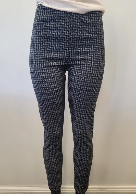 Model wears Bali Corp’s Houndstooth Print Leggings, a high-waisted and comfortable style in classic black and grey, shown from the lower torso down against a plain light wall.