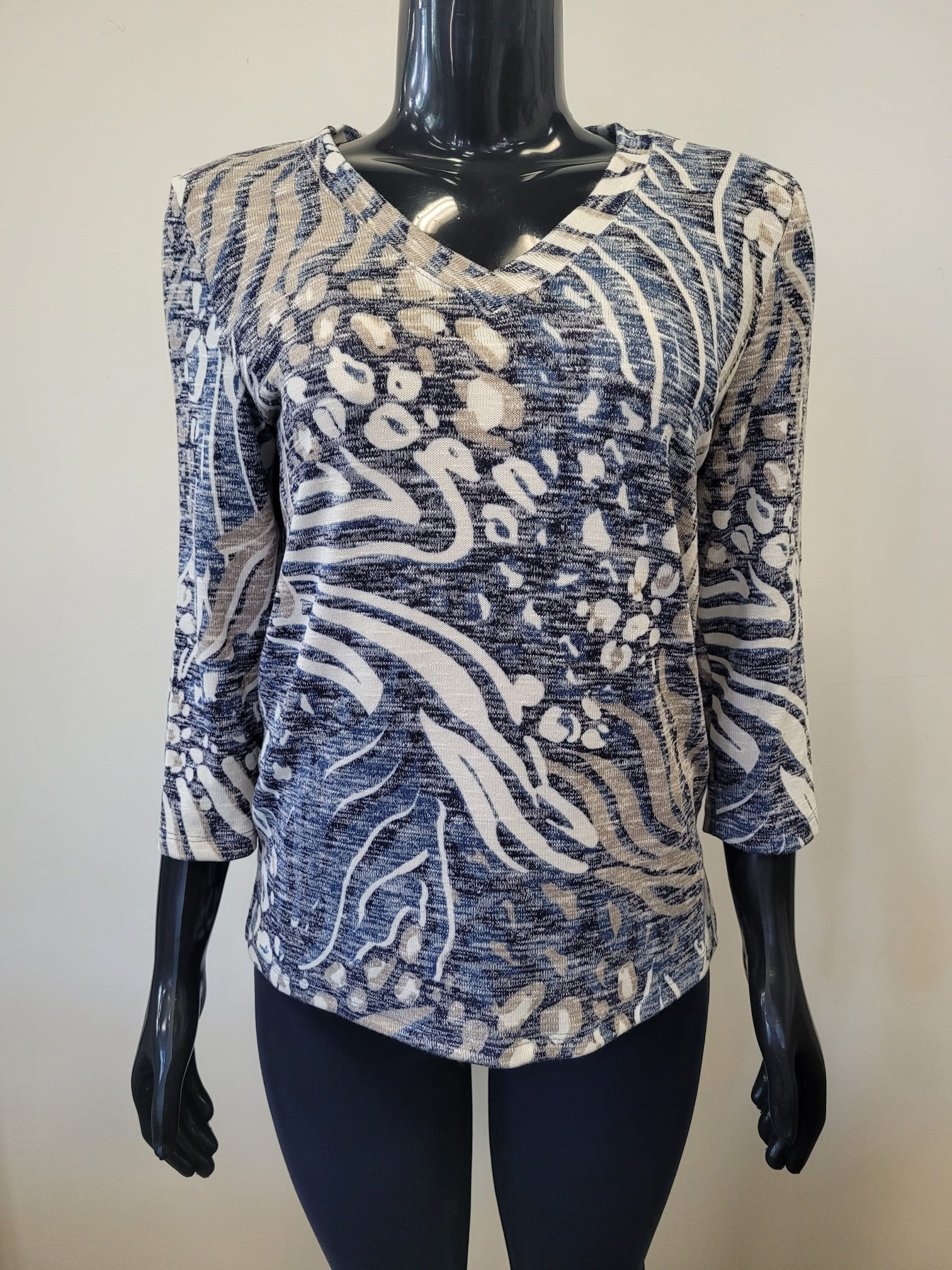 A mannequin showcases the Bali Corp Top-8677, a stylish long sleeve top with a V-neck and abstract white and blue swirling dotted patterns, set against a plain light background.