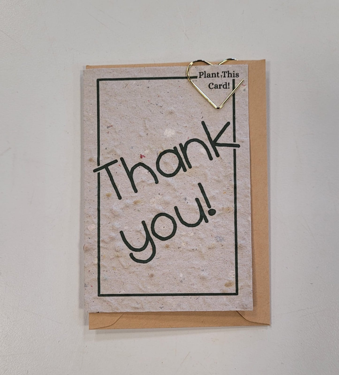 The Mini Greeting Card Seeded Memories by Seeded Memories is a recycled plantable card with "Thank you!" on it, clipped to a brown envelope with a gold heart paperclip. A note at the top says, "Plant This Card!" for an eco-friendly touch.
